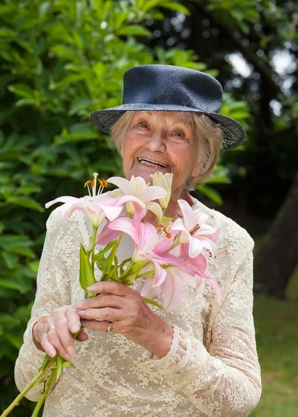 Felice signora anziana con un mazzo di gigli rosa freschi — Foto Stock