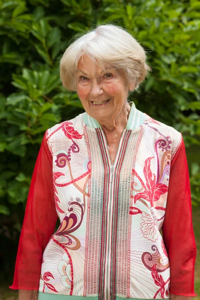 Stijlvolle oudere dame in een rode top in de tuin — Stockfoto