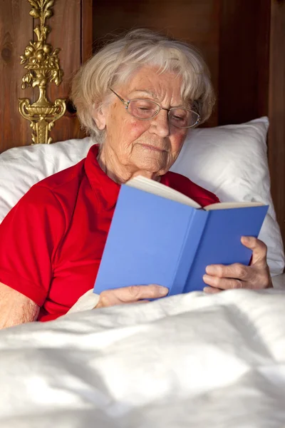 Mujer mayor leyendo un libro en la cama — Foto de Stock