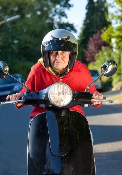 Senior woman riding a scooter crouching low over the handlebars — Stock Photo, Image