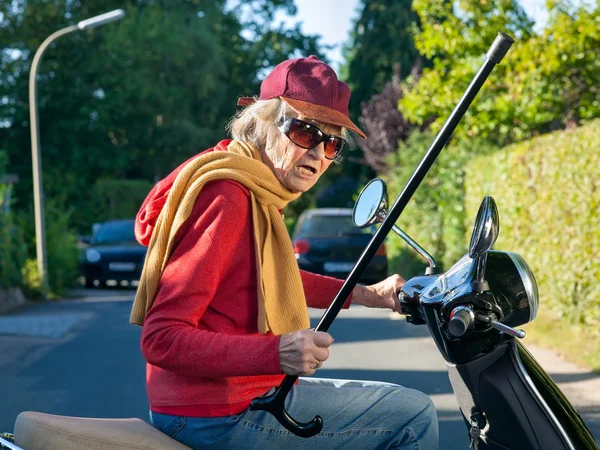 Senior lady riding on a scooter waving her cane — Stock Photo, Image