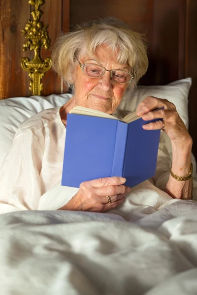 Yaşlı kadın yatakta kitap okuma Stok Fotoğraf