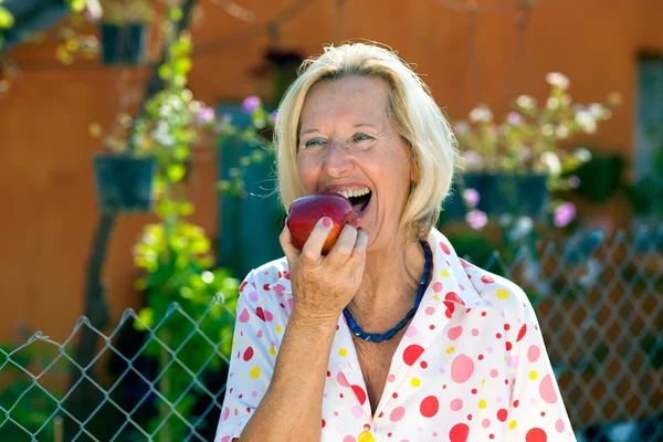 Riendo mujer mayor comiendo una manzana roja . — Foto de Stock