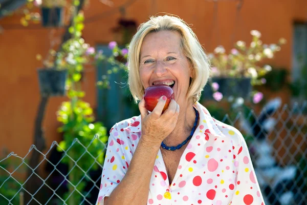 赤いリンゴを楽しんで快活な年配の女性. — ストック写真