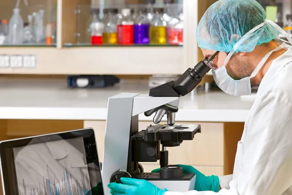 Cientista usando um computador e microscópio . — Fotografia de Stock