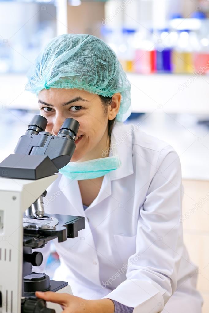 Friendly female lab technician using a microscope. 