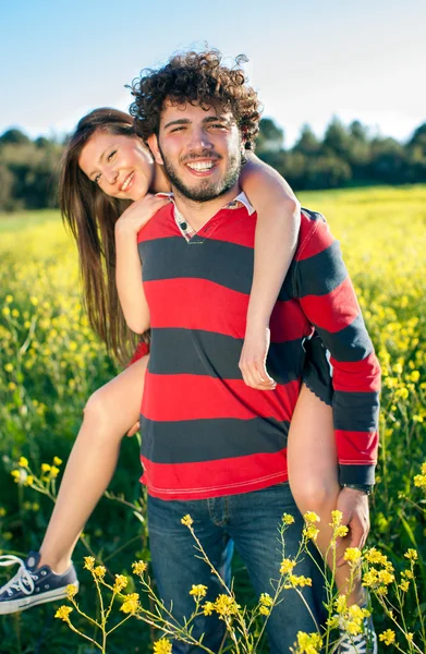 Piggy back ride through rapeseed flowers — Stock Photo, Image