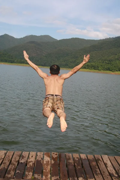 マウンテン ビューの背景を持つ湖の水にジャンプするアジアの男 — ストック写真