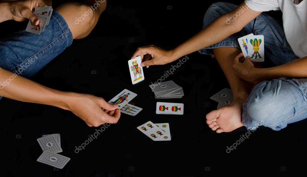 Two boys playing cards on black floor at night Stock Photo by