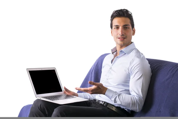 Hombre joven mostrando ordenador portátil sentado en el sofá . — Foto de Stock