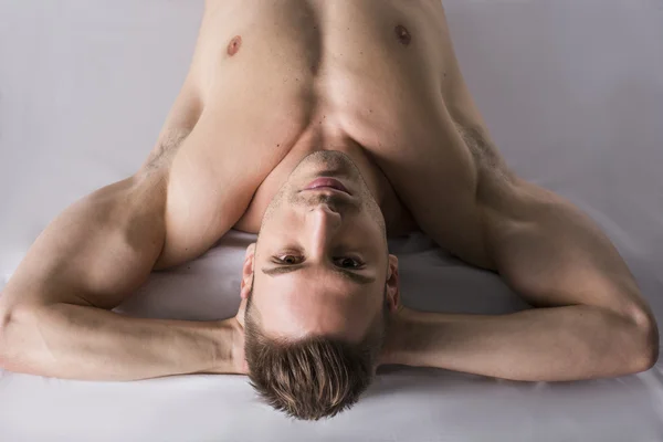 Shirtless young man leaning on white sheet. Hands under his head — Stock Photo, Image