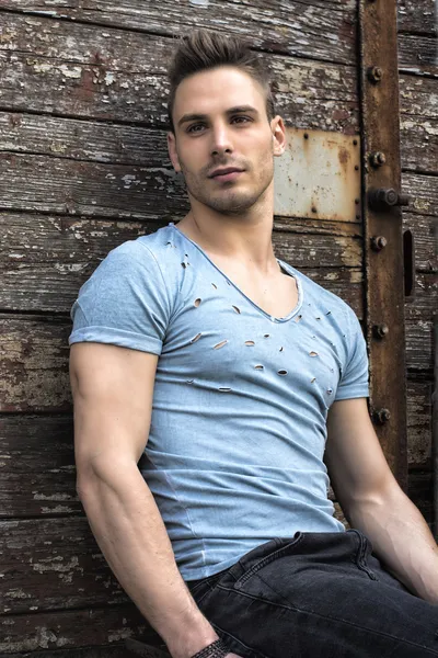 Young man sitting against old wood wall — Stock Photo, Image