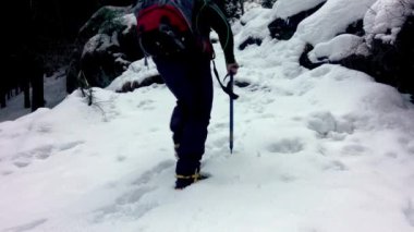 Dağcı adam buz baltasıyla karlı bir yamaca tırmanıyor (Kazma) ve kramponlar