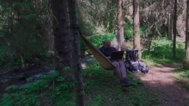 Man with laptop relaxing in hammock and networking in the country