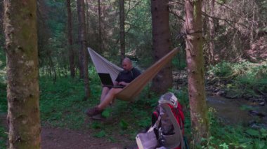 Man with laptop relaxing in hammock and networking in the country