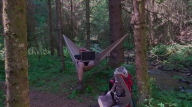 Man with laptop relaxing in hammock and networking in the country
