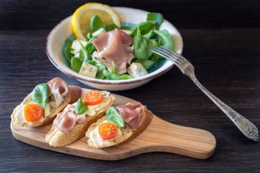 Bruschettas with prosciutto, mozzarella and cherry tomatoes on a wooden cutting board, closeup. Italian style cuisine.	
