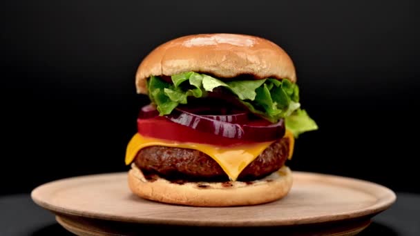 小さな木のまな板で提供され 暗い背景に回転する新鮮な食材とおいしい自家製の牛肉バーガー クローズアップビュー — ストック動画