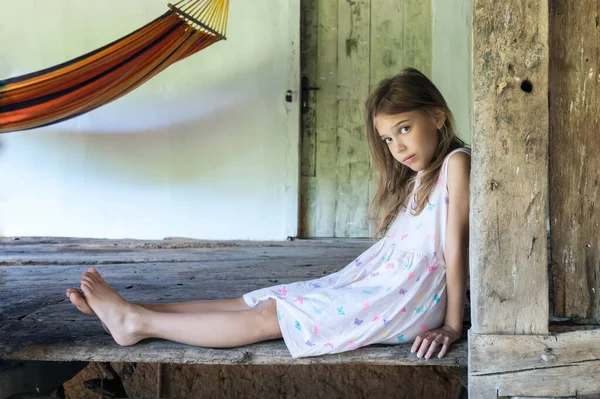 Ahşap zemini olan eski bir kır evinin terasında çıplak ayaklı güzel bir kızın klasik portresi.