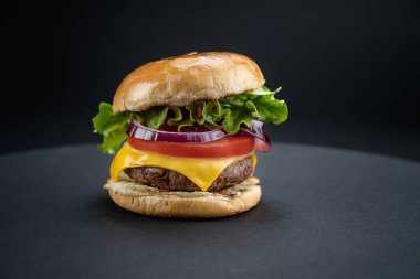 Tasty homemade beef burger with fresh ingredients served on little wooden cutting board with french fries on dark background, close-up view.	