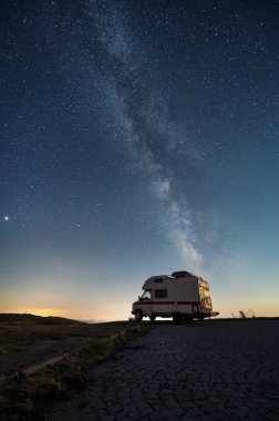 Amazing view of a camper van on the background of a starry night sky with Milky Way galaxy 