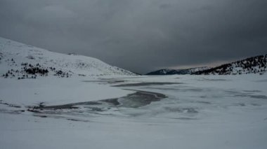 Bulgaristan 'ın Rila Dağları' ndaki Belmeken barajı, donmuş karla kaplı dağ gölü üzerinde ağır bulutların hareket ettiği hızlandırılmış video 