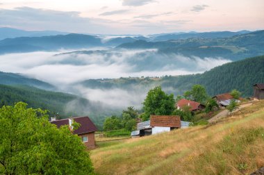Dağ yamaçlarında süzülen güzel alçak bulutların arka planındaki küçük dağ kulübeleriyle muhteşem manzara, Bulgaristan 'da güneş doğarken Rodoplar