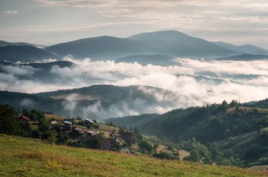 Dağ yamaçlarında süzülen güzel alçak bulutların arka planındaki küçük dağ kulübeleriyle muhteşem manzara, Bulgaristan 'da güneş doğarken Rodoplar