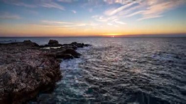 Güneşin doğuşuyla kayalık güzel bir sahil şeridinde hızlandırılmış video.