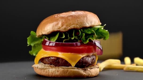 美味的自制牛肉汉堡包 配以新鲜的配料 旁边的薯条在黑暗的背景下旋转着 特写镜头 慢镜头 — 图库视频影像