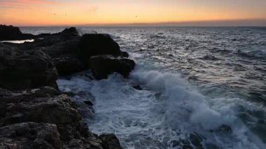 Amazing video with the sun rising, sea waves and a beautiful rocky coast. Slow motion.