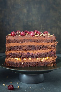 Gri arka planda kirazlı taze yapılmış lezzetli bir çikolatalı pasta. Yarım pasta. Kesilmiş kekin görünür katmanları ve dolgusu var. Doğum günü pastası. Boşluğu kopyala.