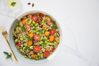 Domatesli kinoa tabbouleh, edamame, kırmızı soğan, maydanoz ve kabak çekirdeği. Sağlıklı bir vejetaryen yemek kasesi.