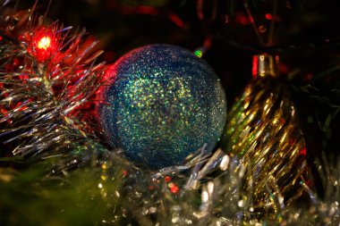 Çam ağacında yeşil bir top ya da Noel ağacı dalında. Koyu arkaplan ve kırmızı ışıklı çelenk. Yumuşak odak