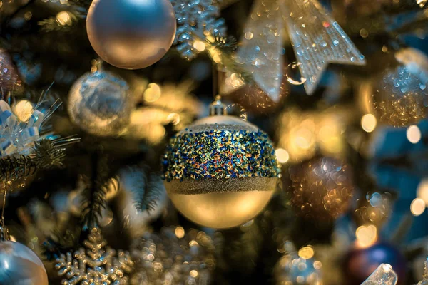 Weihnachtsbaum und goldene festliche Glaskugeln mit farbigem Funkeln, wunderschönes gelbes Bokeh aus leuchtenden Girlanden. Unklarer Hintergrund. — Stockfoto
