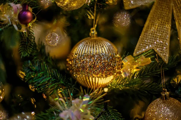 Goldene festliche Glaskugel mit farbigen Funkeln, Weihnachtsbaum und wunderschönem gelben Bokeh aus leuchtenden Girlanden. Unklarer Hintergrund. — Stockfoto
