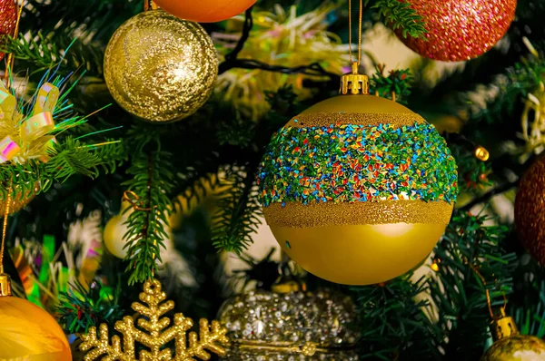 Goldene festliche Glaskugel mit farbigem Funkeln, Schneeflocke am Weihnachtsbaum und gelbem Bokeh aus glühender Girlande. — Stockfoto