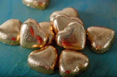 Eski yeşil bir masada altın folyoyla yapılmış kalp şeklinde çikolatalar. Bulanık koyu arka plan. Düğün kartı. Yumuşak odak.