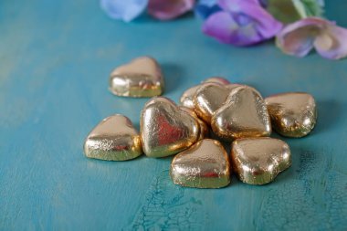 Eski yeşil bir masada altın folyoyla yapılmış kalp şeklinde çikolatalar. Çiçeklerle bulanık bir arkaplan. Düğün kartı. Yumuşak odak.