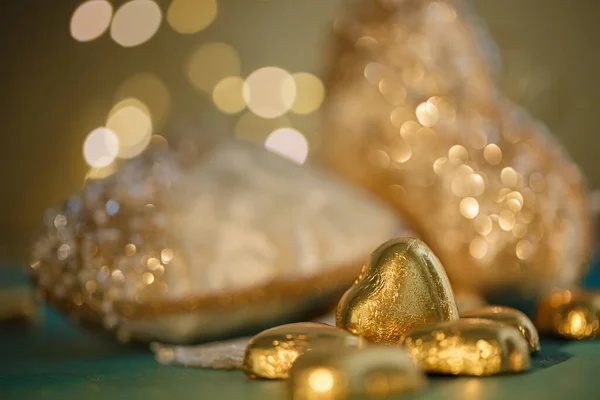 Heart shaped chocolates in golden foil on a green table. Blurred beige hearts with bokeh. Wedding greeting card. Soft focus. Royalty Free Stock Images