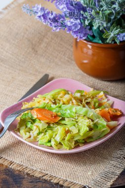 Pembe bir tabakta kızartılmış lahana, havuç, soğan, çatal ve bıçakla pişirilmiş bir masa örtüsü..