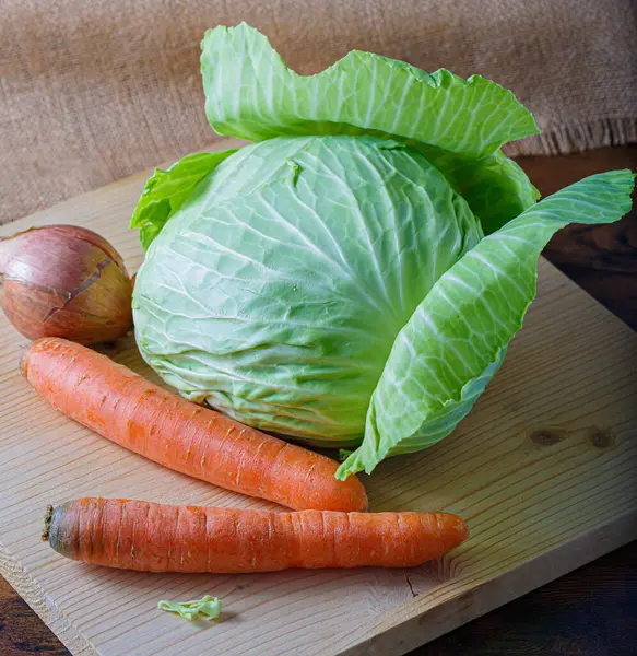 Las verduras frescas crudas la zanahoria, la cebolla con la cáscara y la col blanca con las hojas verdes sobre la tabla de madera. Comida vegetariana saludable. — Foto de Stock