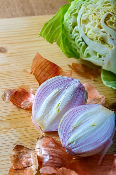 Primer plano de cebolla morada con cáscara y col blanca en una tabla de madera. Verduras frescas crudas cortadas en dos partes. Enfoque suave. —  Fotos de Stock