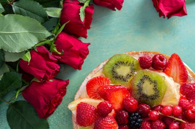 Düz kırmızı çiçekler ve yeşil arka planda böğürtlenli lezzetli bir pasta. Tebrik kartı