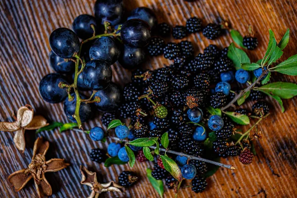 Üst manzara böğürtlen üzümleri ahşap bir masada. Yeşil yapraklar ve kuru çiçekler. Yüzeyin derinliği. Karanlık, bulanık bir arkaplan. Yumuşak odak.