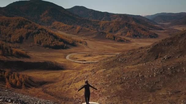 Республіка Алтай, Сибір, Росія. Безкоштовна мандрівниця підкидає руки і насолоджується безконечним пейзажем зі змієподібною автострадою - величезними горами. Повітряний вид прекрасної осінньої дикої природи — стокове відео