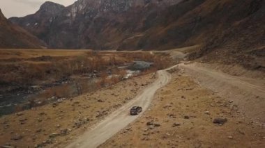 Büyük bir dağ köpüren nehri olan Katu-Yaryk kanyonu Chulyshman Vadisi 'nde boş bir köy yolunda siyah bir SUV aracı sürüyor. Altai, Sibirya, Rusya. İnsanlar kir içinde seyahat eder.