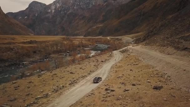 Um carro de jipe SUV preto está dirigindo ao longo de uma estrada rural vazia no enorme canyon Katu-Yaryk Chulyshman Valley com um grande rio borbulhante de montanha. Altai, Sibéria, Rússia. As pessoas viajam ao longo de uma terra — Vídeo de Stock