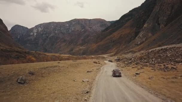 黒いSUVのジープ車は、大きな山の泡の川と巨大なカトゥヤーク峡谷チュリーシュマン渓谷の空の田舎道に沿って運転しています。アルタイ、シベリア、ロシア。土の上を旅する — ストック動画