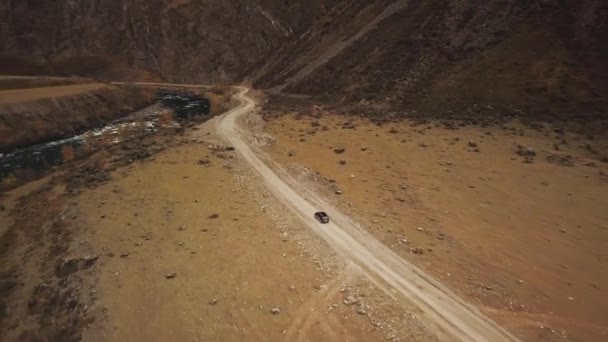 Egy fekete terepjáró egy üres országúton halad végig a hatalmas Katu-Yaryk kanyonban a Chulyshman-völgyben egy nagy hegyi buborékos folyóval. Altai, Szibéria, Oroszország. Az emberek a mocsokban utaznak. — Stock videók